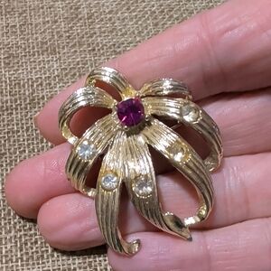 gold-tone flower brooch with a purple/pink center stone and rhinestone accents